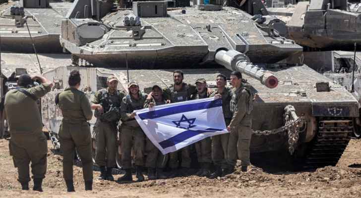 “Israeli” soldiers pose for a picture with a tank positioned near the border with the Gaza Strip (May 9, 2024) (Photo: Ahmad Gharabli/AFP)