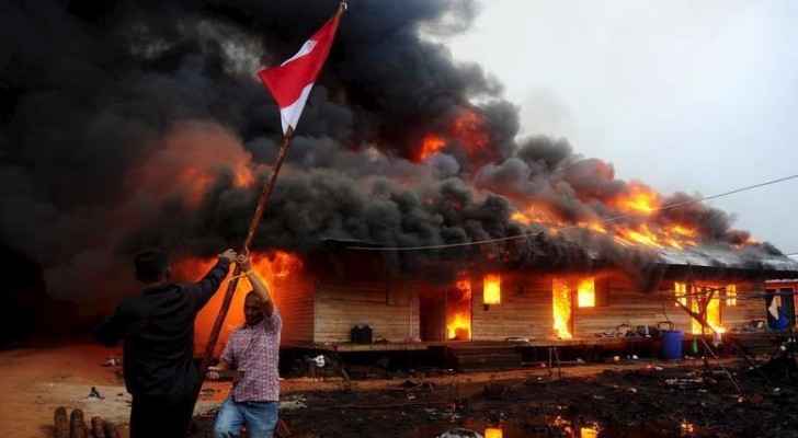 Two villagers remove the flag after others burned down the compound of a religious group. (Photo Courtesy: Reuters)