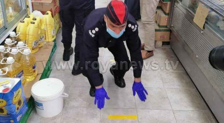 Police officers draw distance floor-markers to urge people in Mafraq practice social distancing