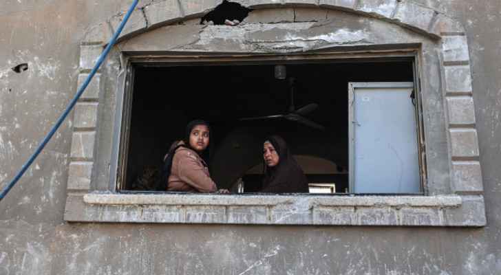 Two Palestinians gaze out from a window of a house targeted in an "Israeli" airstrike in Khan Yunis